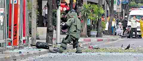 Bystanders watch as a bomb disposal expert approaches the attack site in Bangkok