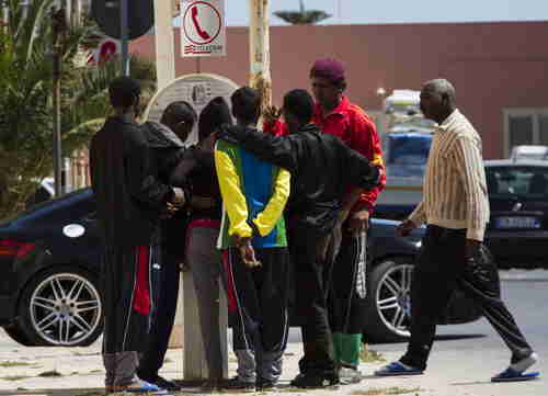 Migrants queue at phone booth on the Island of Lampedusa, Southern Italy, on Thursday (AP)