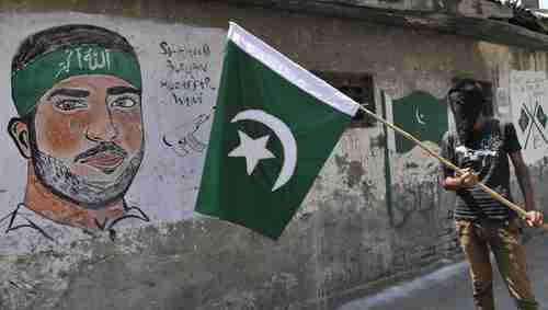 A masked Kashmir protester in Kashmir on Sunday waves a Pakistan flag next to a graffiti of Hizbul Mujahideen commander Burhan Muzaffar Wani.  Wani was shot and killed by police on July 8, triggering weeks of riots, demonstrations and violence since then.  (Hindustan Times)
