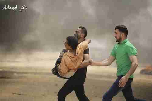 A child is carried by Palestinians away from the front lines after he was shot.  The smoke is created by burning tires that the Palestinians use to hide from the Israel troops (Ma'an News)