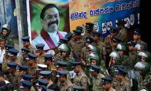  Sri Lankan police and special forces stand guard next to a poster of the newly appointed prime minister, Mahinda Rajapaksa (Reuters)