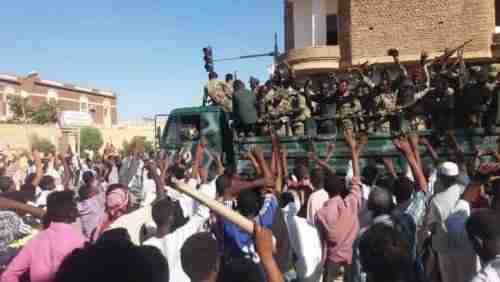Anti-government protesters in Atbara, Sudan, on 20-Dec wave their hands at security forces (Sudan Tribune)