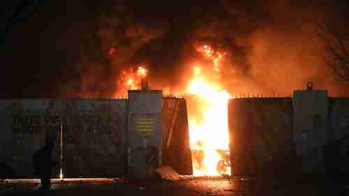 Hijacked cars burn at the Peace Wall as rioting broke out in West Belfast, Northern Ireland on Wednesday (AP)