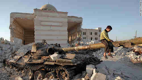 A boy plays on the gun of a destroyed Syrian army tank partially covered in the rubble of the destroyed Azaz mosques north of Aleppo (CNN)