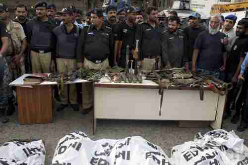 Police display confiscated suicide vests and heavy weapons brought in by the terrorists.  In the foreground are the dead bodies of the terrorists in white sacks (AP)
