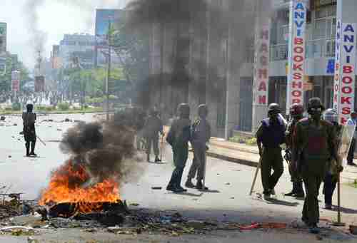 Police officers walk past burning tyres in Kisumu, Kenya, on Monday (AFP)