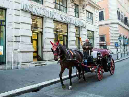 A horse-drawn carriage passes a branch of Banca Monte dei Paschi bank in Rome.